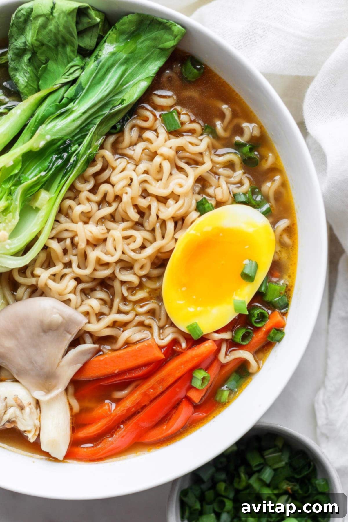 A vibrant bowl of ramen, richly topped with a perfectly halved black tea and ginger ramen egg, showcasing its jammy yolk.