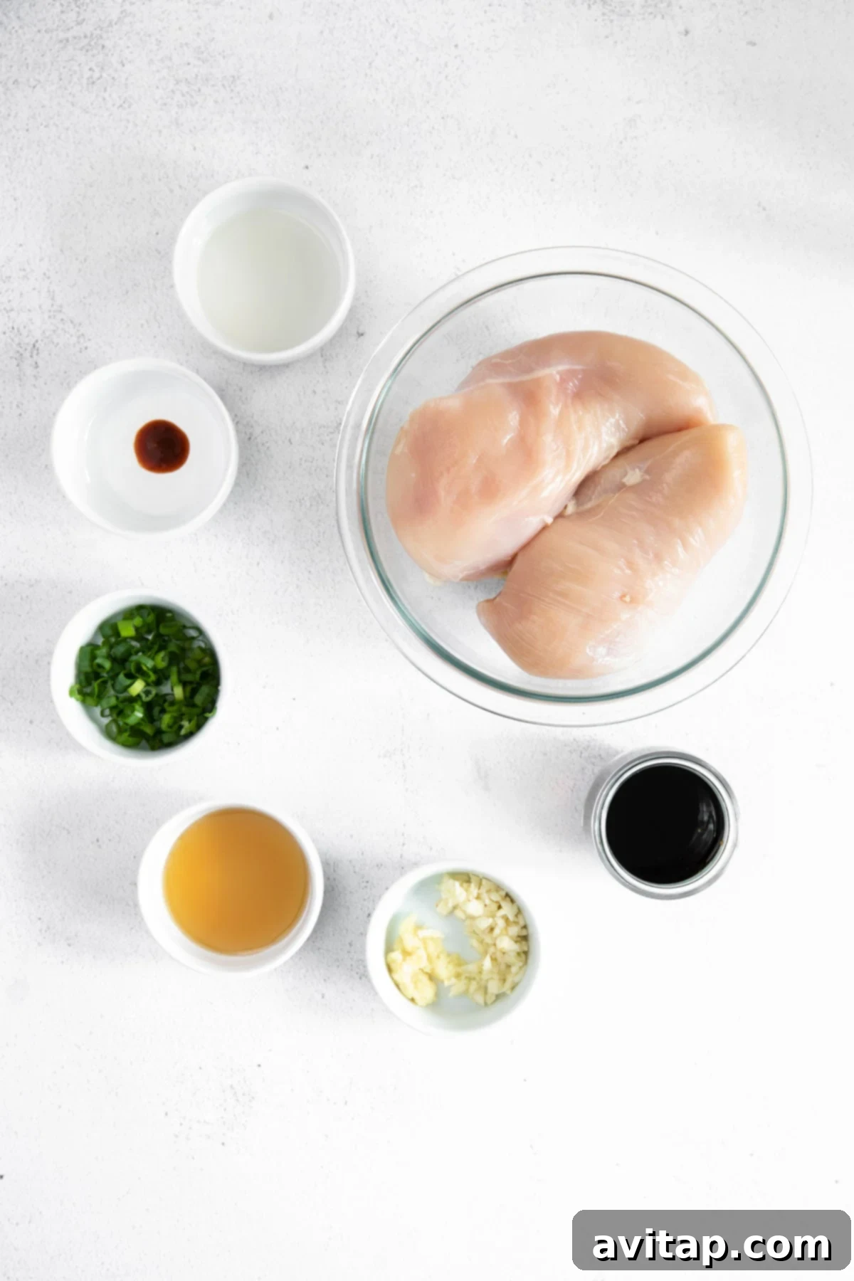 Fresh ingredients for homemade teriyaki chicken marinade laid out on a clean countertop, including soy sauce, ginger, garlic, sriracha, maple syrup, green onions, and rice vinegar