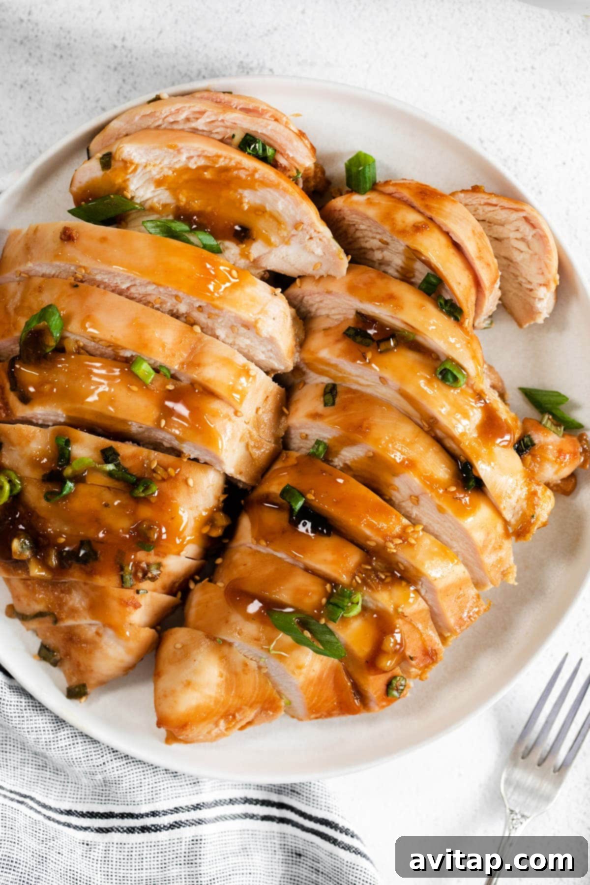 Finely sliced baked teriyaki chicken breast arranged on a plate, garnished with sesame seeds and fresh green onions