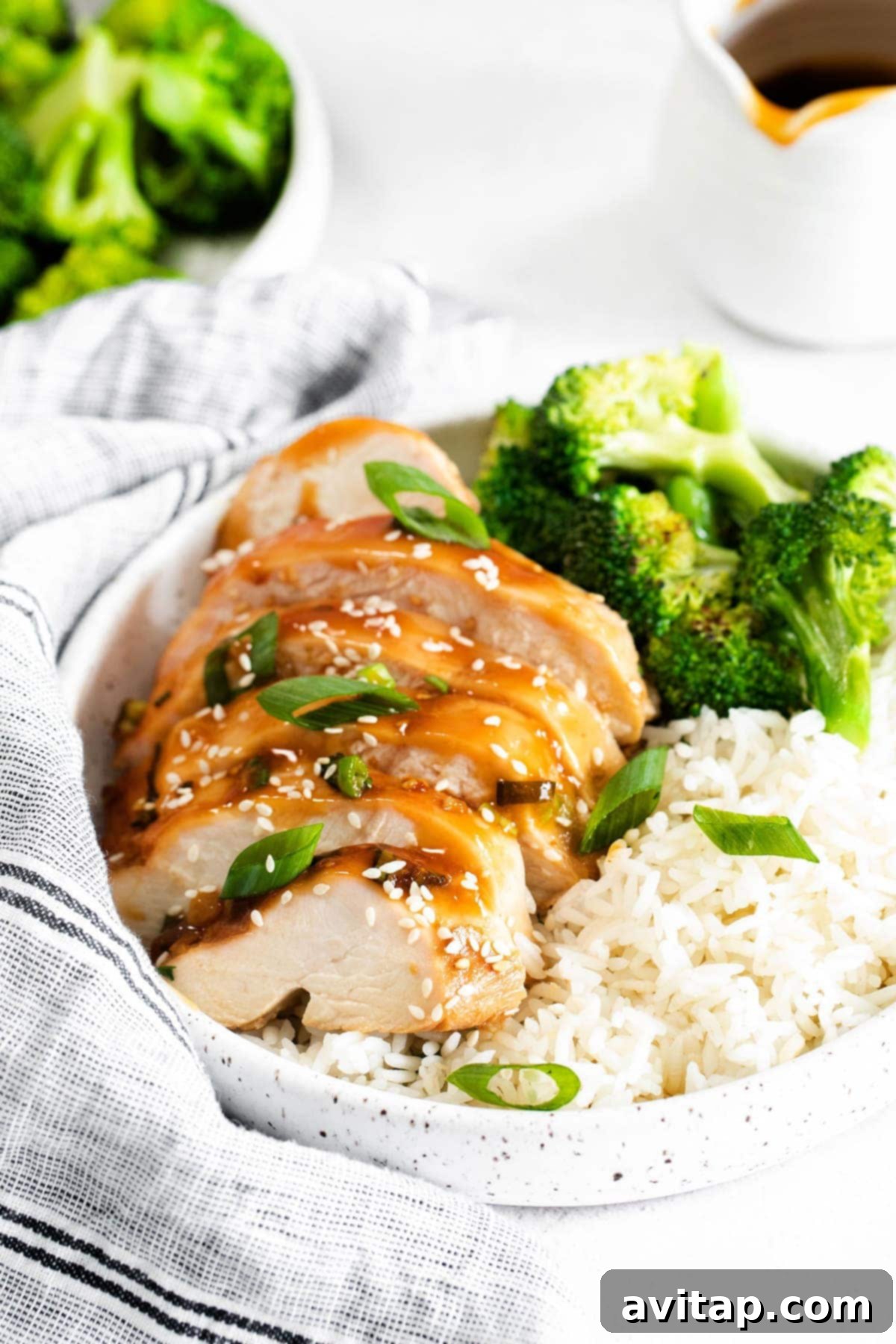 A bowl of sliced teriyaki chicken breast served with white rice and steamed broccoli, ready to eat