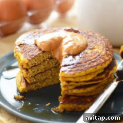 A stack of perfectly cooked gluten-free pumpkin pancakes, invitingly presented with a dusting of powdered sugar and a side of maple syrup, capturing the warm essence of fall.