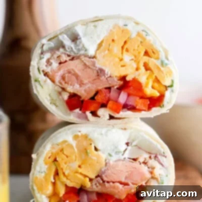 A perfectly wrapped smoked salmon breakfast burrito, showcasing a delicious filling of fluffy scrambled eggs, fresh green onions, tender smoked salmon, and a creamy, tangy spread, all encased in a warm tortilla.