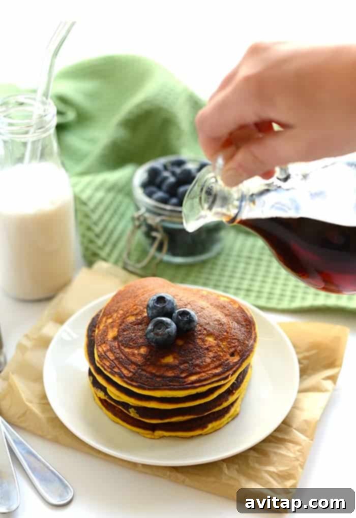 A stack of perfectly golden-brown Paleo Coconut Flour Pancakes, topped with fresh berries and maple syrup, ready to be enjoyed. The texture promises ultimate fluffiness.