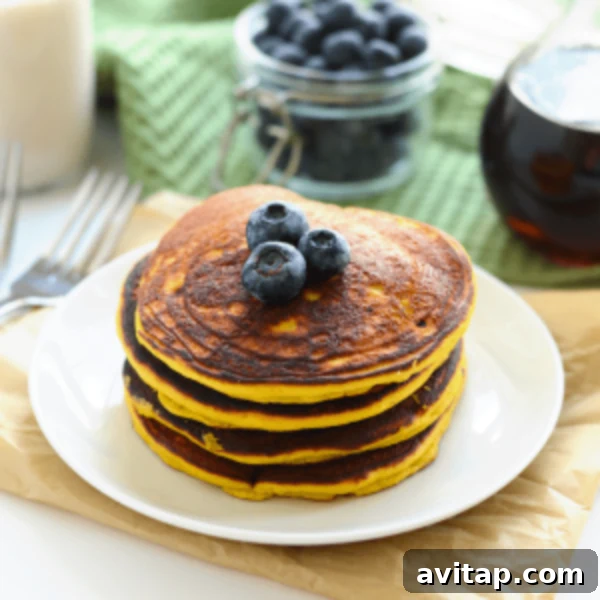 A stack of golden Paleo Coconut Flour Pancakes with fresh blueberries on top, served on a white plate, ready for breakfast.