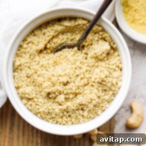 This 5-Ingredient Vegan Parmesan Cheese is a delicious vegan alternative to traditional grated parmesan. Make a batch and sprinkle onto any savory dish your heart desires. A small bowl filled with homemade vegan parmesan cheese, garnished with a sprig of rosemary.