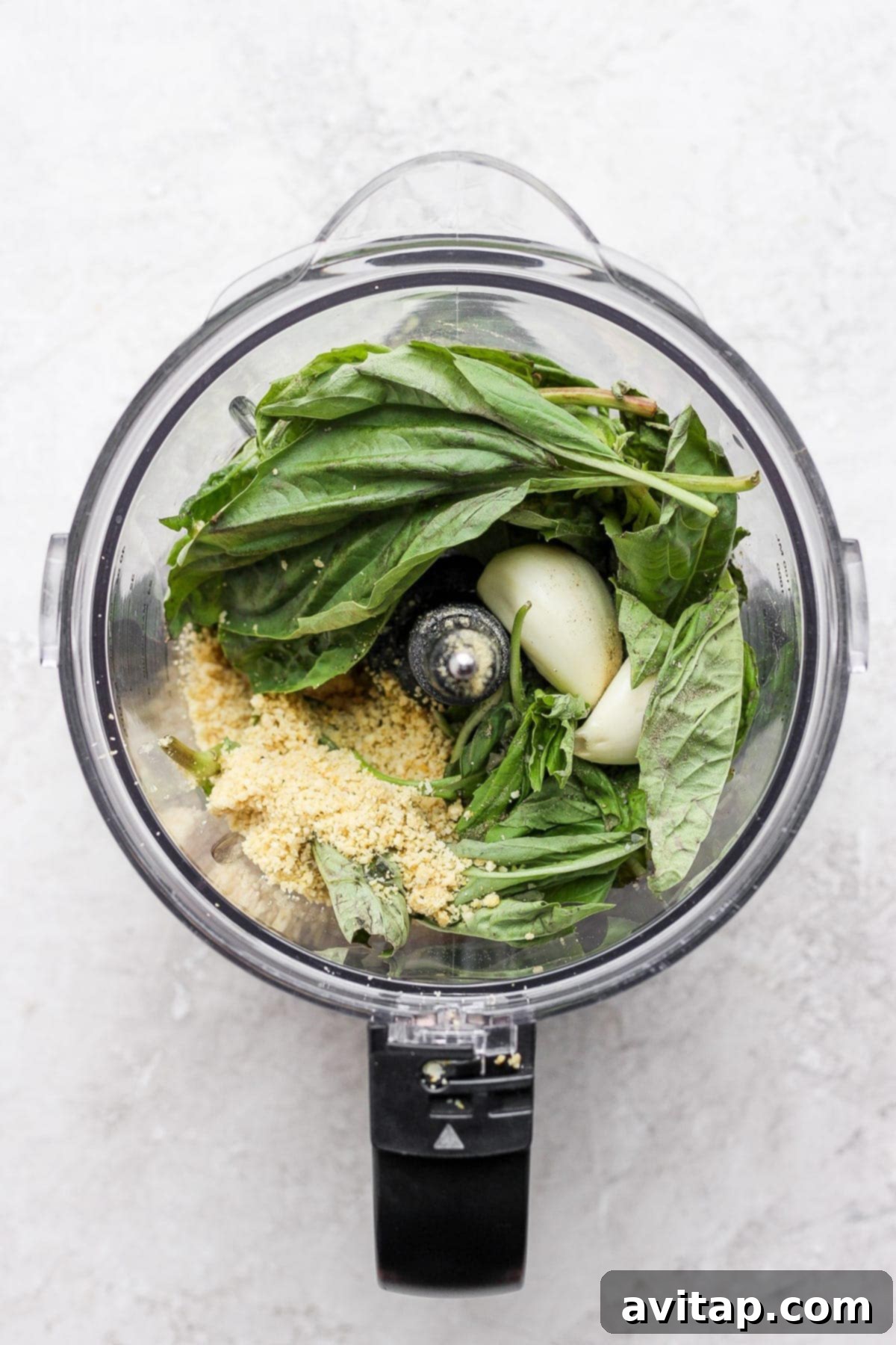 Make this simple vegan pesto recipe with fresh basil, olive oil, lemon juice, and a homemade vegan parmesan cheese. Ingredients for vegan pesto, including fresh basil, olive oil, lemon, garlic, and vegan parmesan, in a food processor, ready for blending.