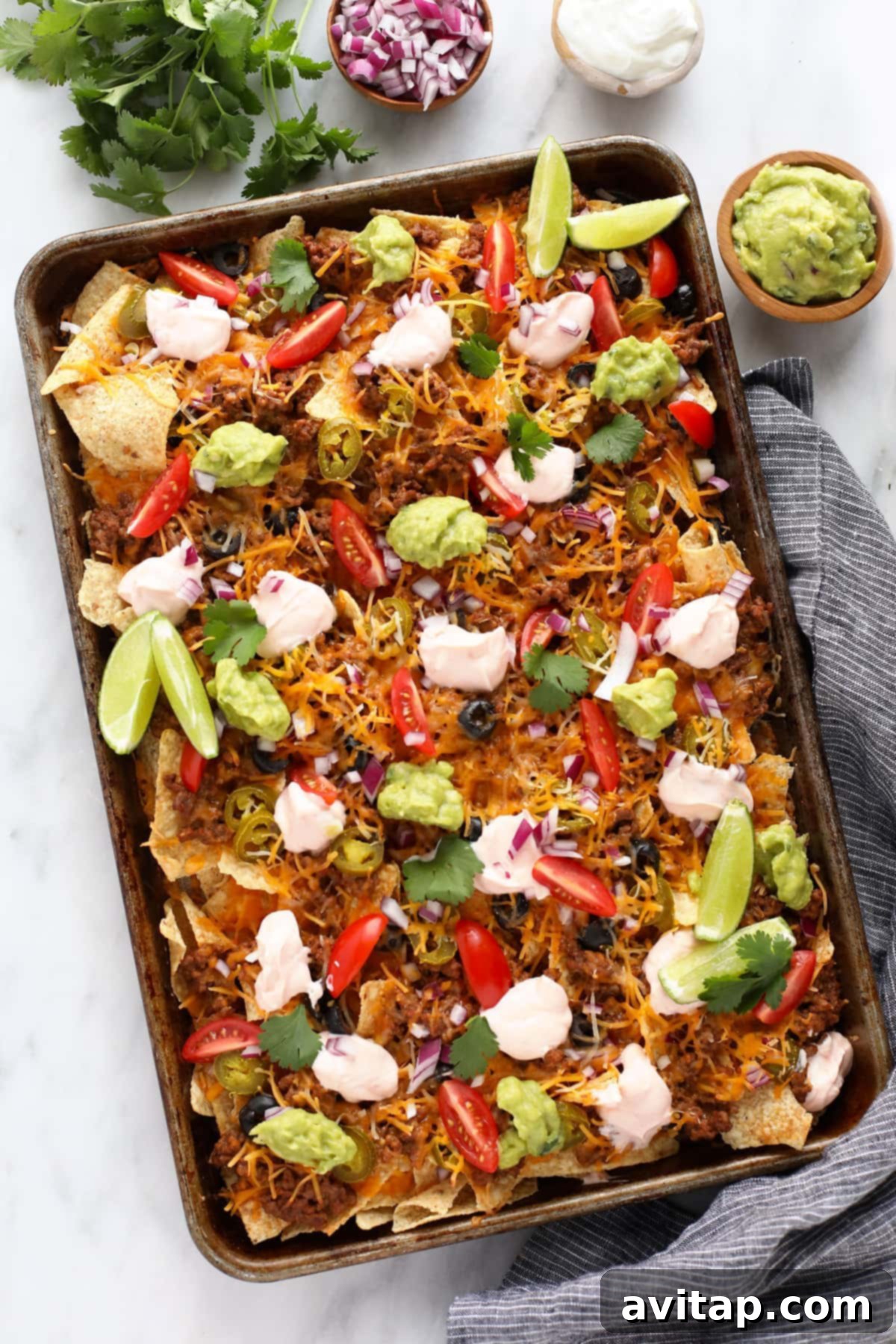 Delicious Ground Beef Nachos, a perfect quick dinner or game day appetizer. A large baking sheet filled with ground beef nachos, generously topped with melted cheese, guacamole, and other fresh ingredients, ready to be served.