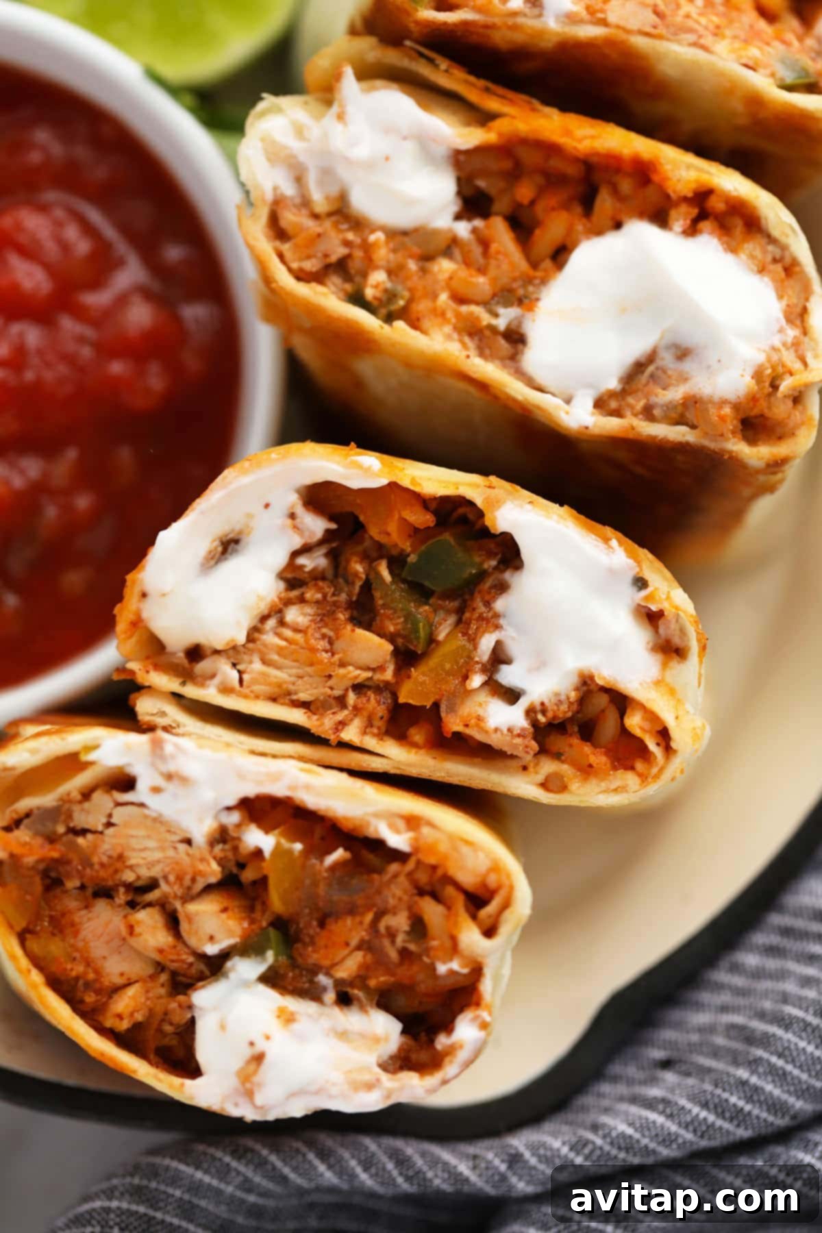 Two easy shredded chicken burritos, cut in half to showcase their savory filling, neatly arranged and topped with a dollop of fresh sour cream.
