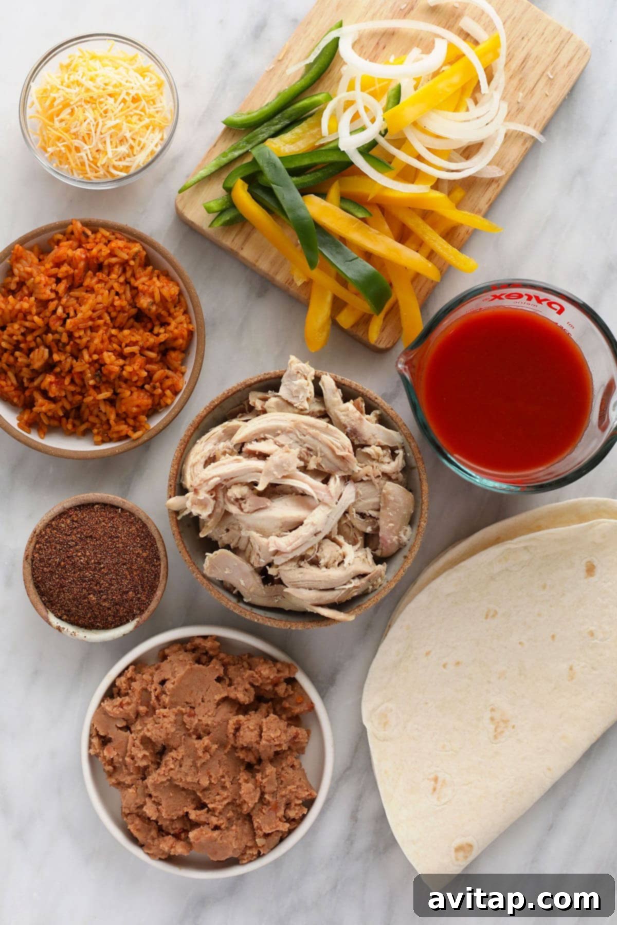 A vibrant selection of fresh and canned ingredients, including bell peppers, onions, shredded chicken, tortillas, and beans, neatly arranged and ready for the assembly of shredded chicken burritos.