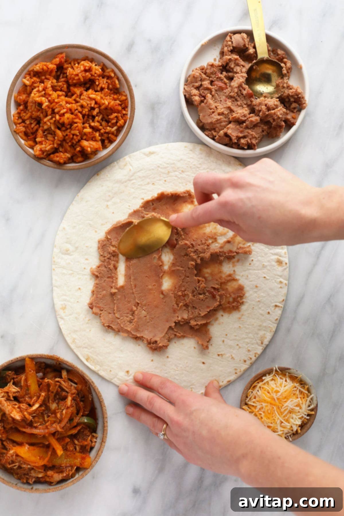 Creamy refried beans being spread evenly across a large flour tortilla with a spoon, forming the flavorful and essential base layer for a shredded chicken burrito.