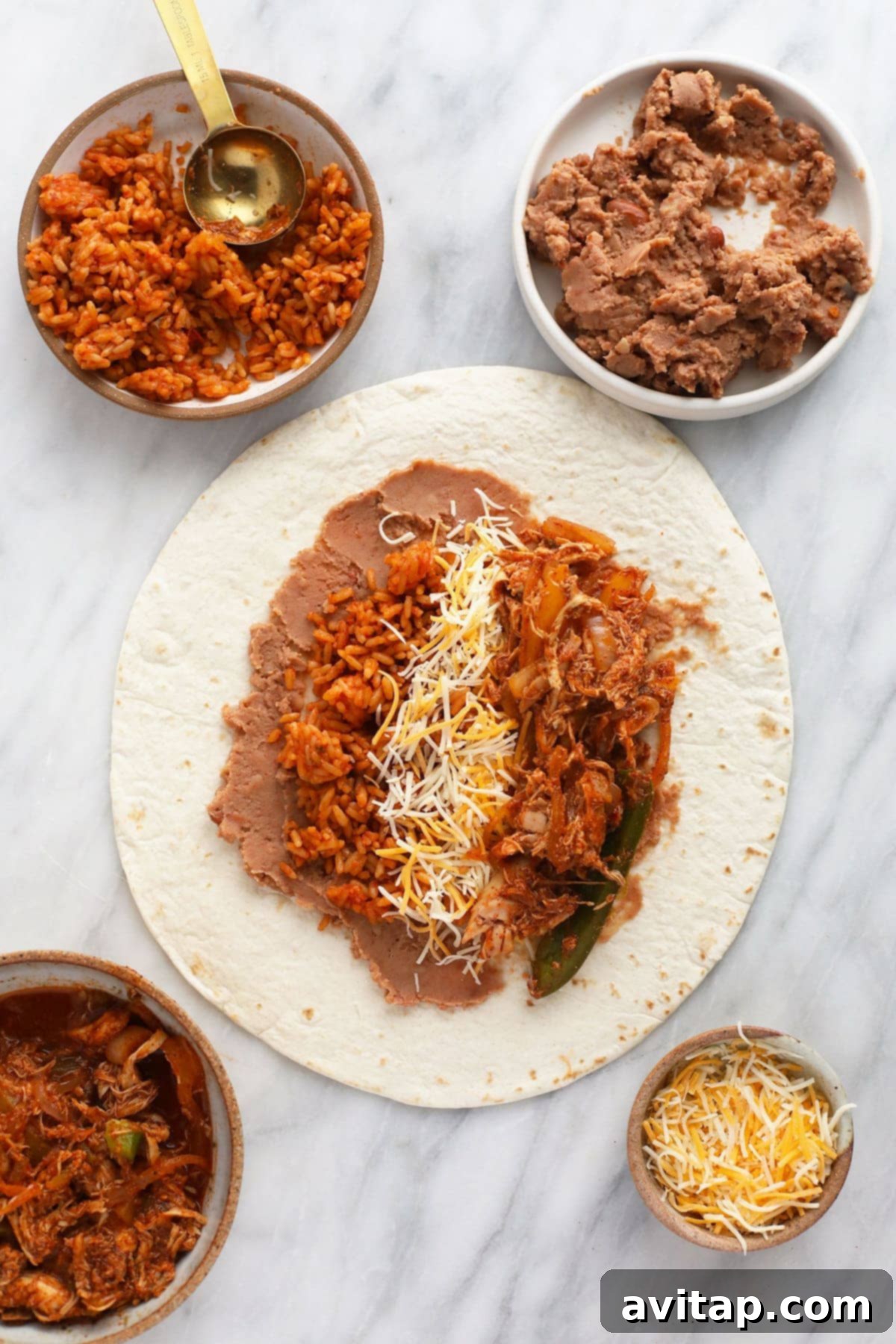 A hand carefully layering shredded chicken, Spanish rice, and cheese onto a refried bean-spread flour tortilla, demonstrating the assembly process for shredded chicken burritos.