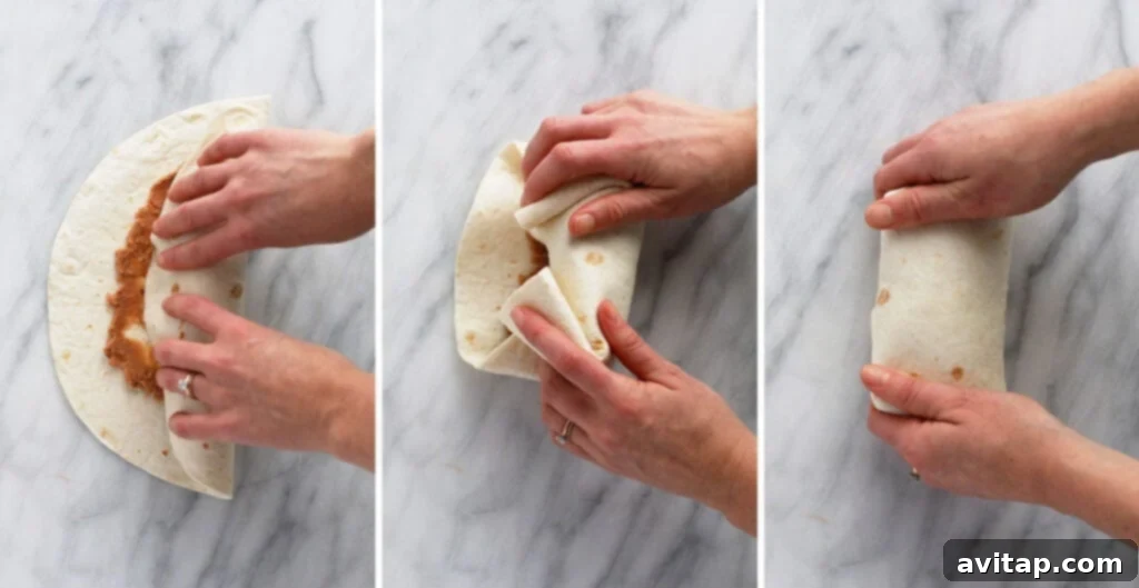 A shredded chicken burrito being expertly rolled up, with the sides neatly folded in and the bottom edge rolled upwards, forming a secure and compact package ready for cooking or freezing.