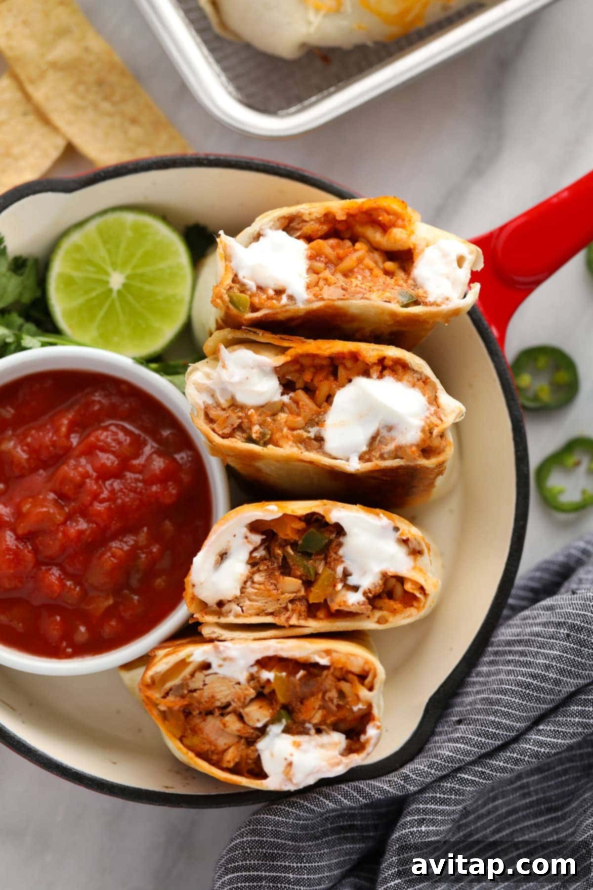 Two freshly prepared and halved shredded chicken burritos, revealing their rich filling, elegantly displayed alongside a small bowl of vibrant red salsa, ready for a delicious meal.