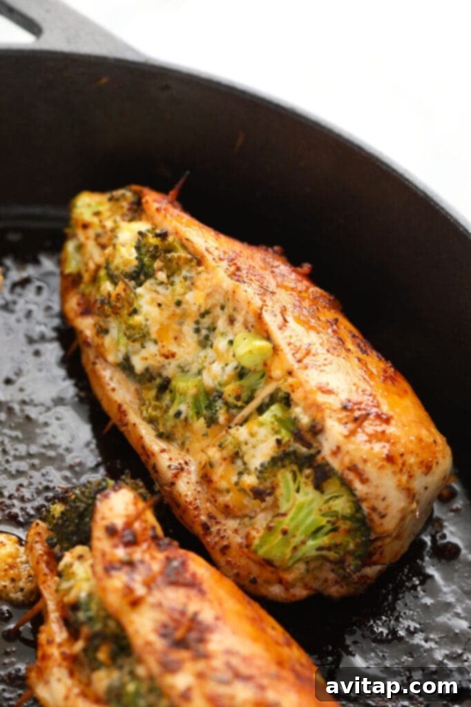 Two perfectly cooked broccoli and cheese stuffed chicken breasts in a cast iron skillet, garnished with fresh herbs.
