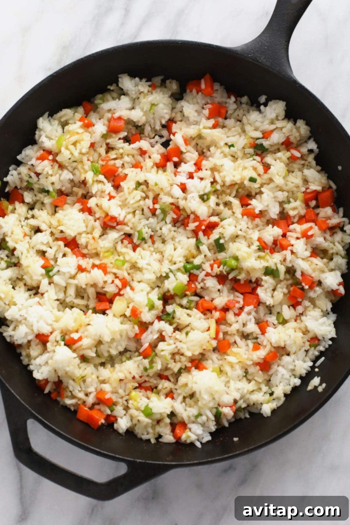 Veggies and rice being stir-fried in a large cast iron pan for chicken fried rice