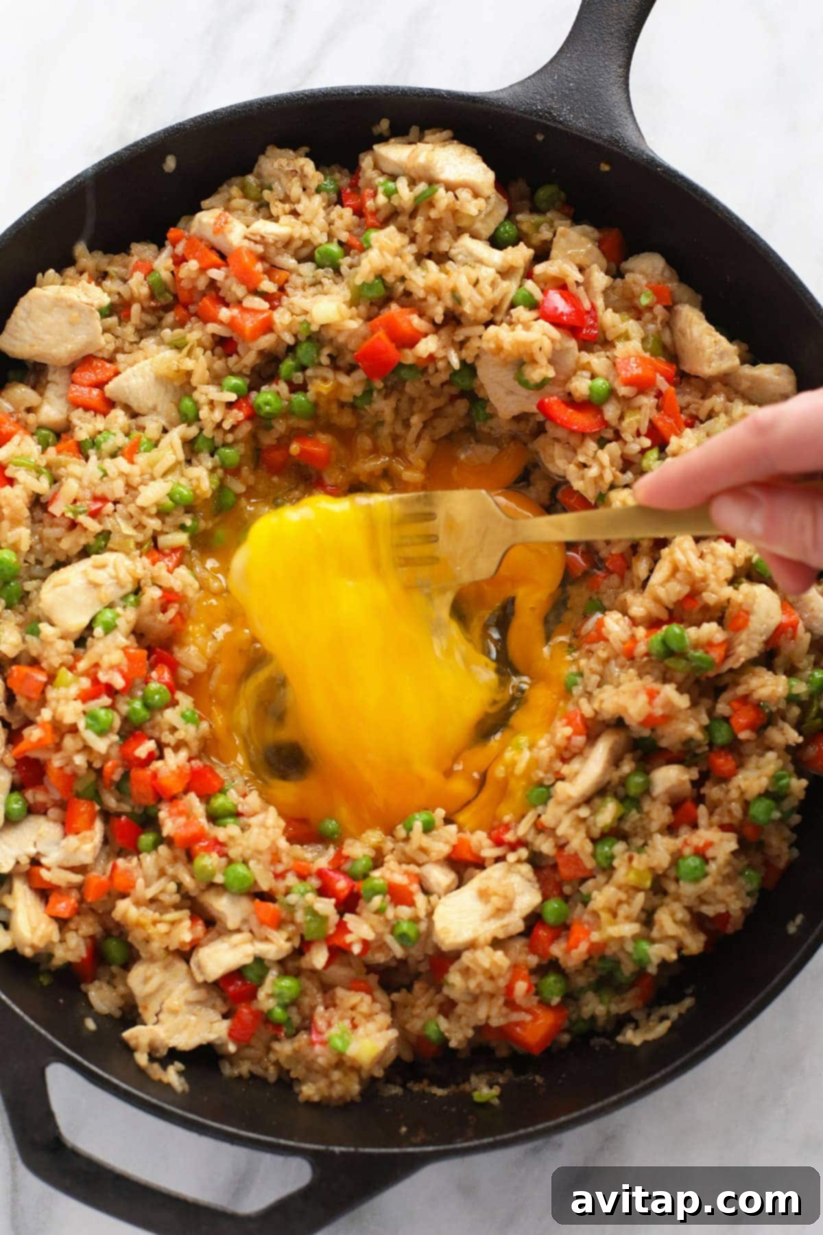 Scrambled eggs being folded into cooked chicken fried rice in a large pan