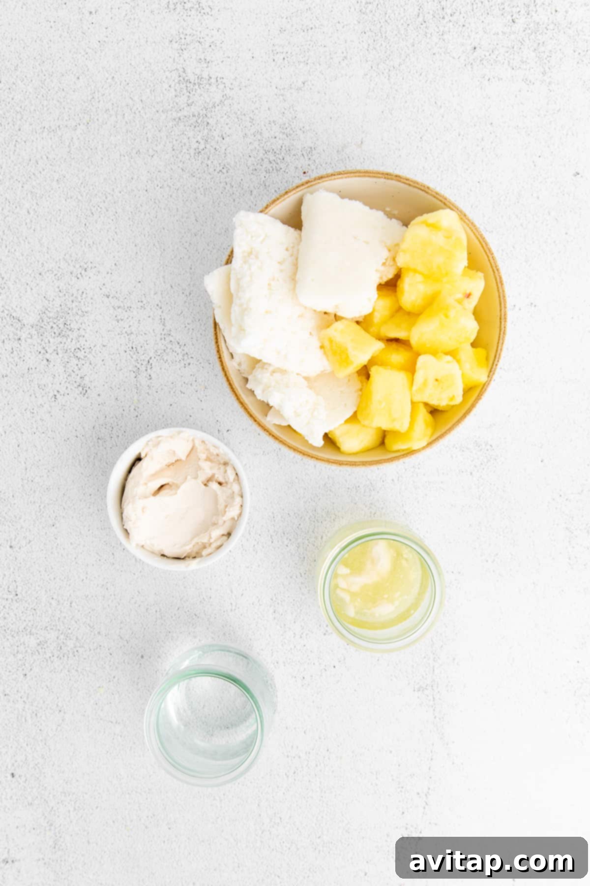 A vibrant selection of piña colada ingredients laid out on a kitchen countertop, including frozen pineapple chunks, creamy coconut meat, a bottle of white rum, and cans of coconut milk.