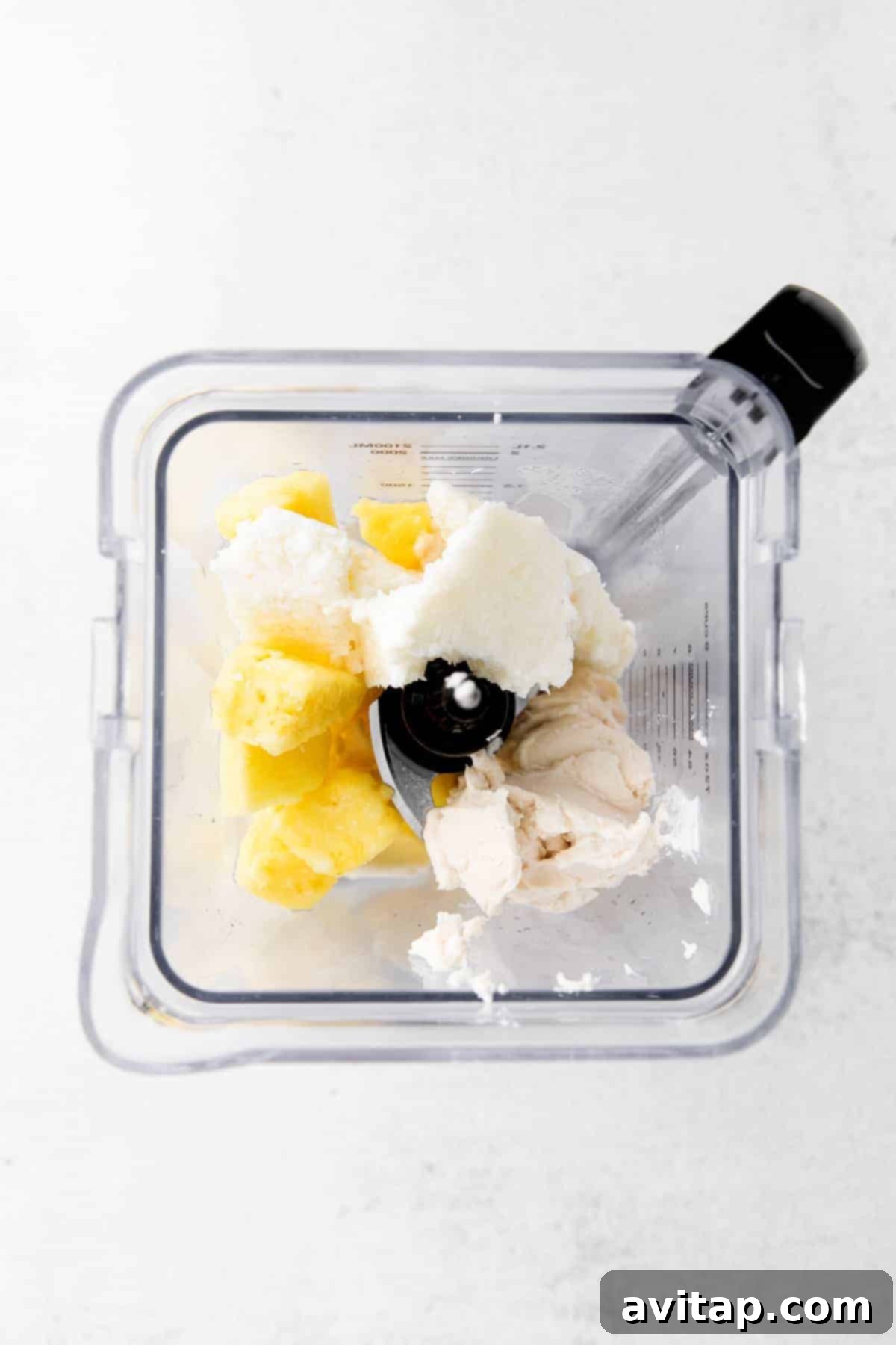 All the piña colada ingredients — frozen pineapple, coconut meat, white rum, and coconut cream — are ready to be blended in a high-speed blender, promising a creamy and refreshing drink.