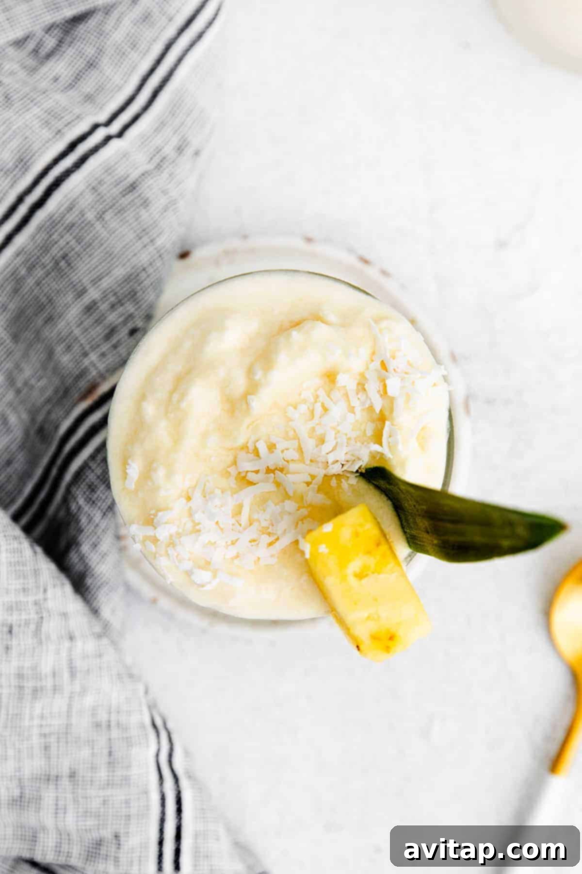 A refreshing piña colada served in a clear glass, garnished with a ripe pineapple chunk on the rim, ready to be enjoyed.