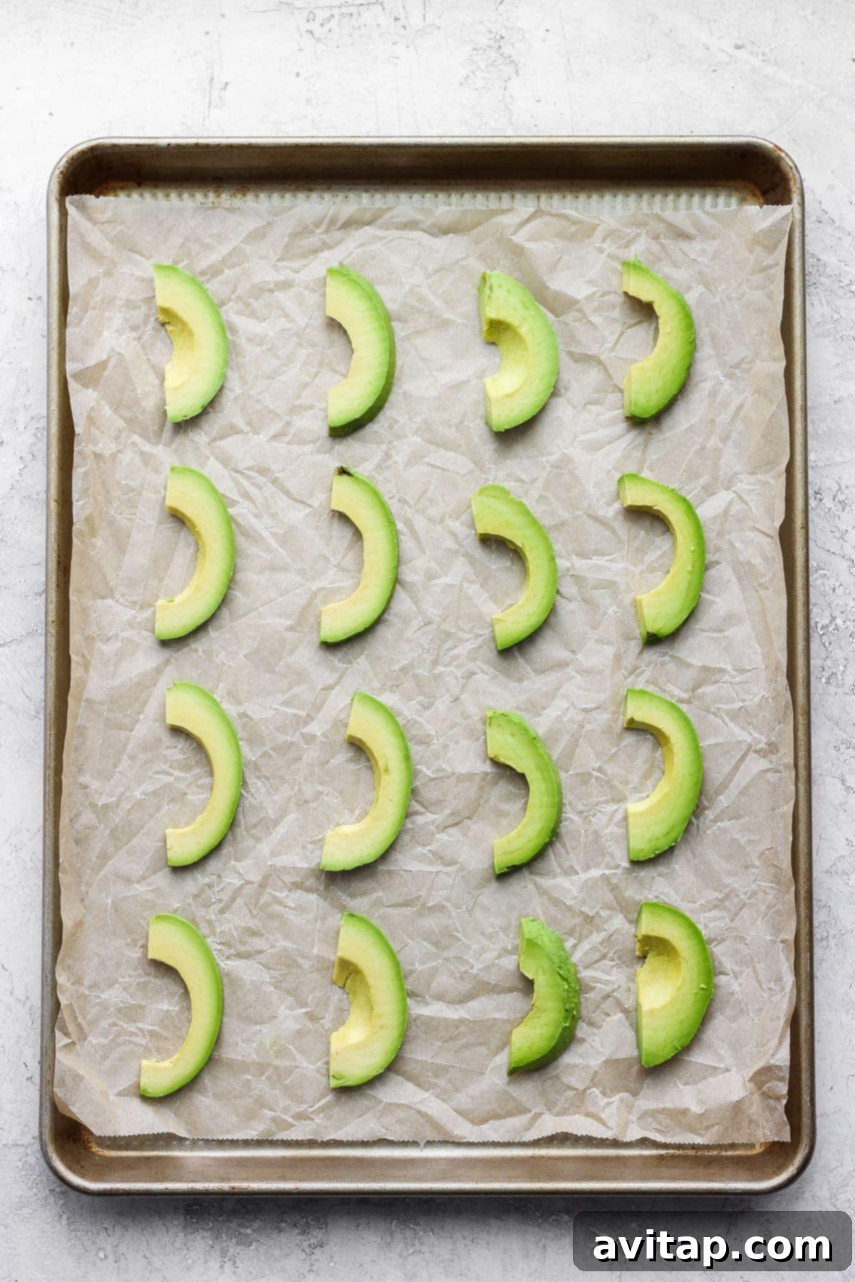 slices of avocado on parchment paper and a baking sheet, ready to be placed in the freezer