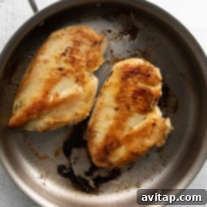 Effortless Creamy Chicken Alfredo 6 Two perfectly cooked chicken breasts, golden-brown and seared, resting in a stainless steel skillet after cooking, with delicious pan drippings visible.