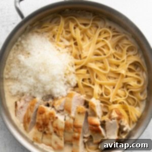 Effortless Creamy Chicken Alfredo 8 Cooked fettuccine pasta being actively tossed with rich, creamy Alfredo sauce in a stainless steel pan, alongside sliced grilled chicken breast and grated Parmesan cheese.
