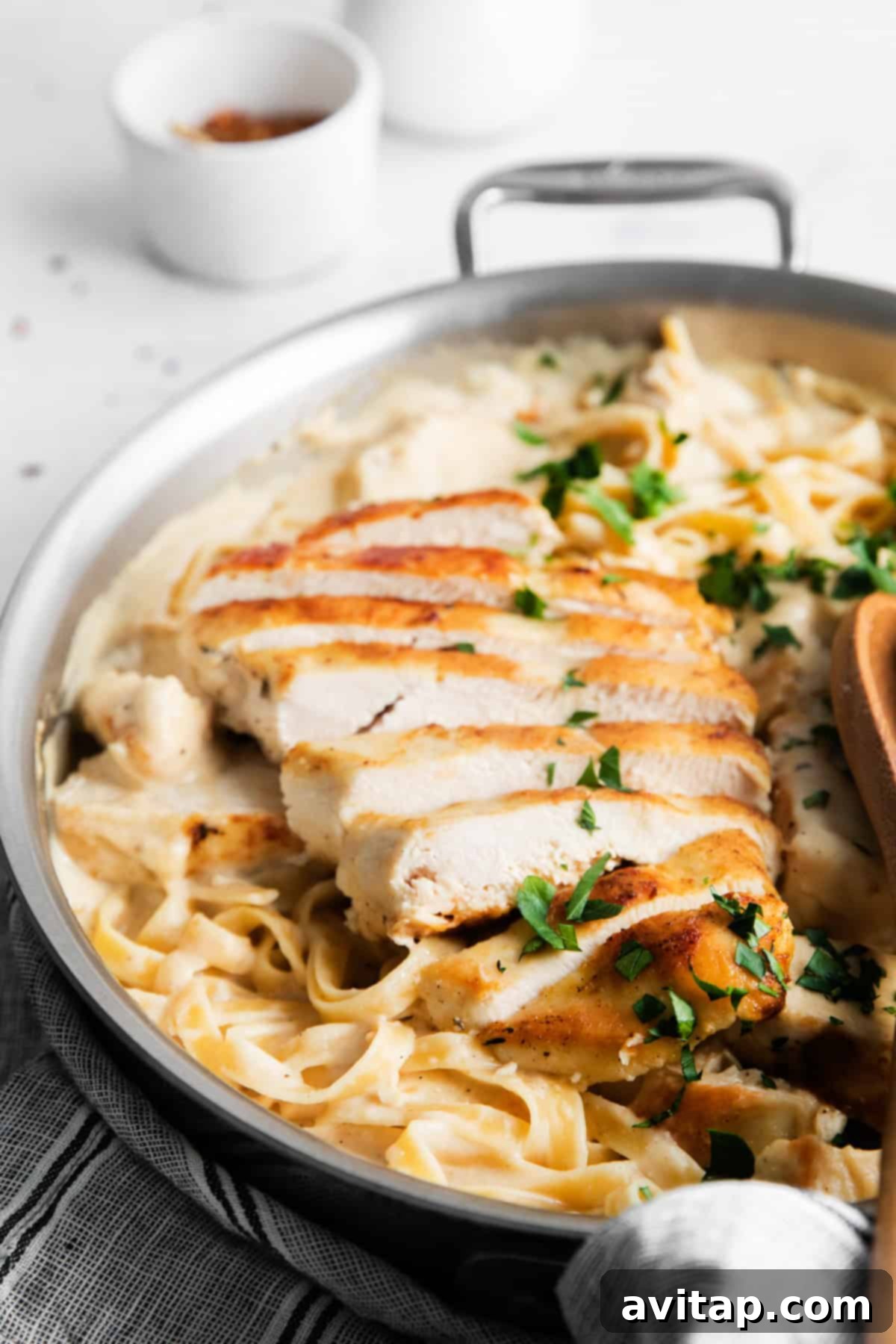 Effortless Creamy Chicken Alfredo 10 A large skillet brimming with creamy fettuccine Alfredo, generously topped with slices of perfectly grilled chicken and adorned with vibrant fresh chopped parsley, poised for serving.