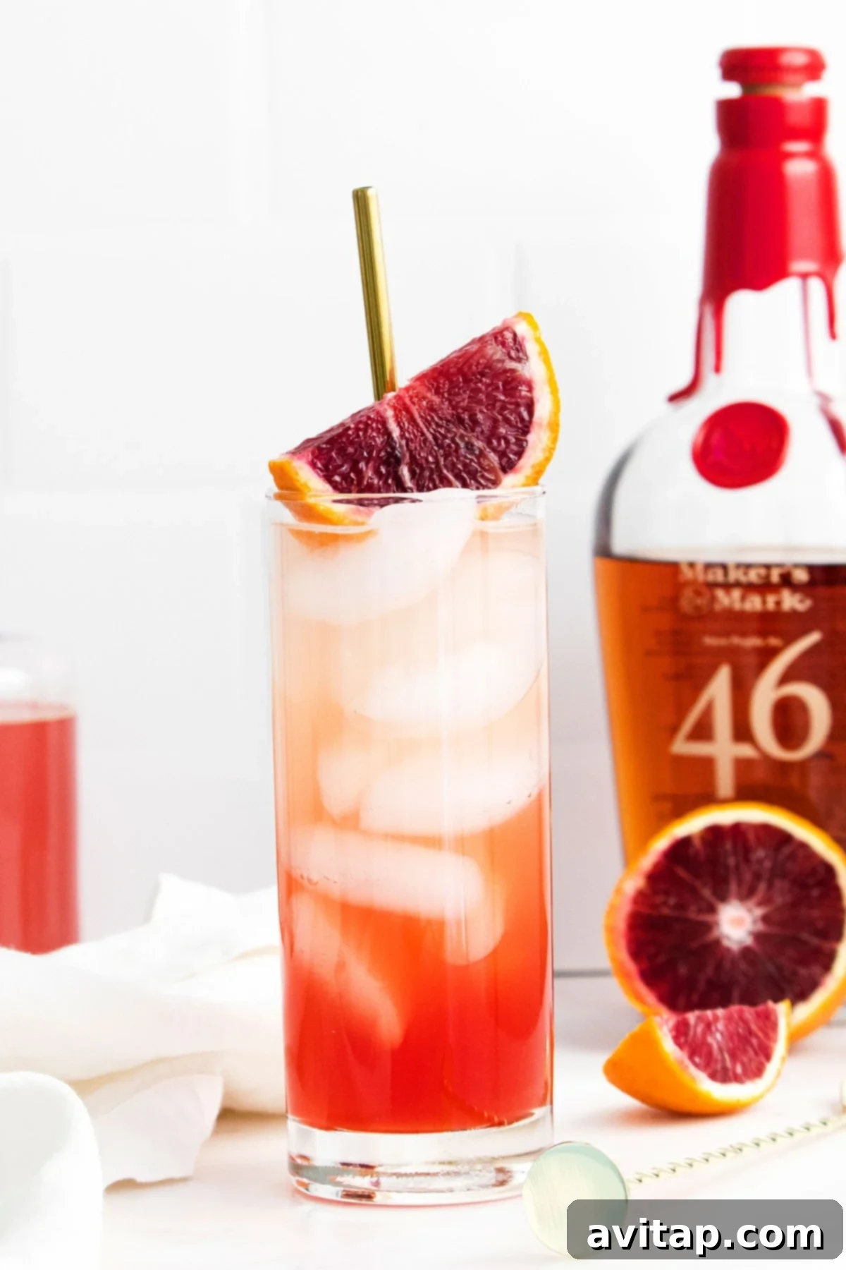 Sanguine Sunset Sip 2 A vibrant Blood Orange Smash cocktail in a glass next to a bottle of bourbon, garnished with a blood orange slice.