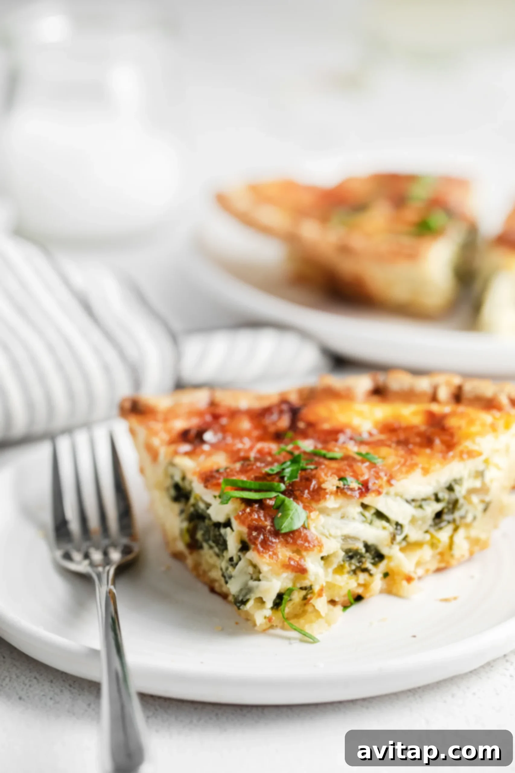 A beautifully presented slice of spinach quiche on a pristine white plate, garnished and ready to be enjoyed.