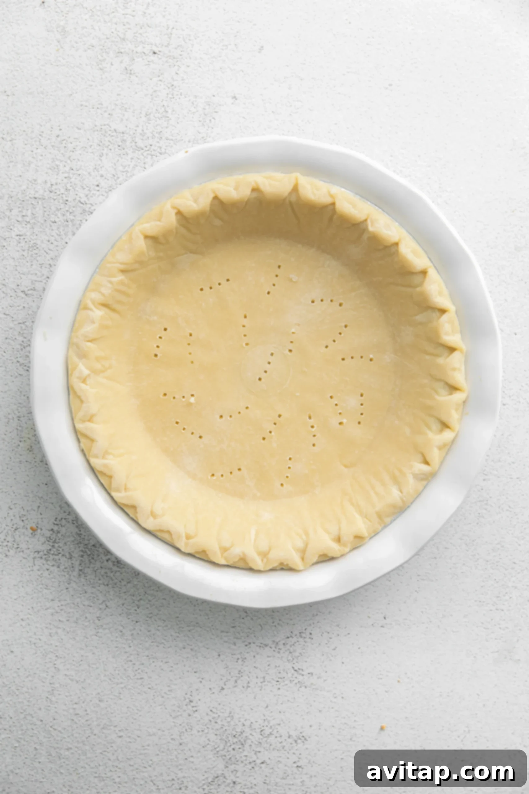 A pre-made pie crust in a pie pan, meticulously pricked with a fork to prevent bubbling during the blind baking process.