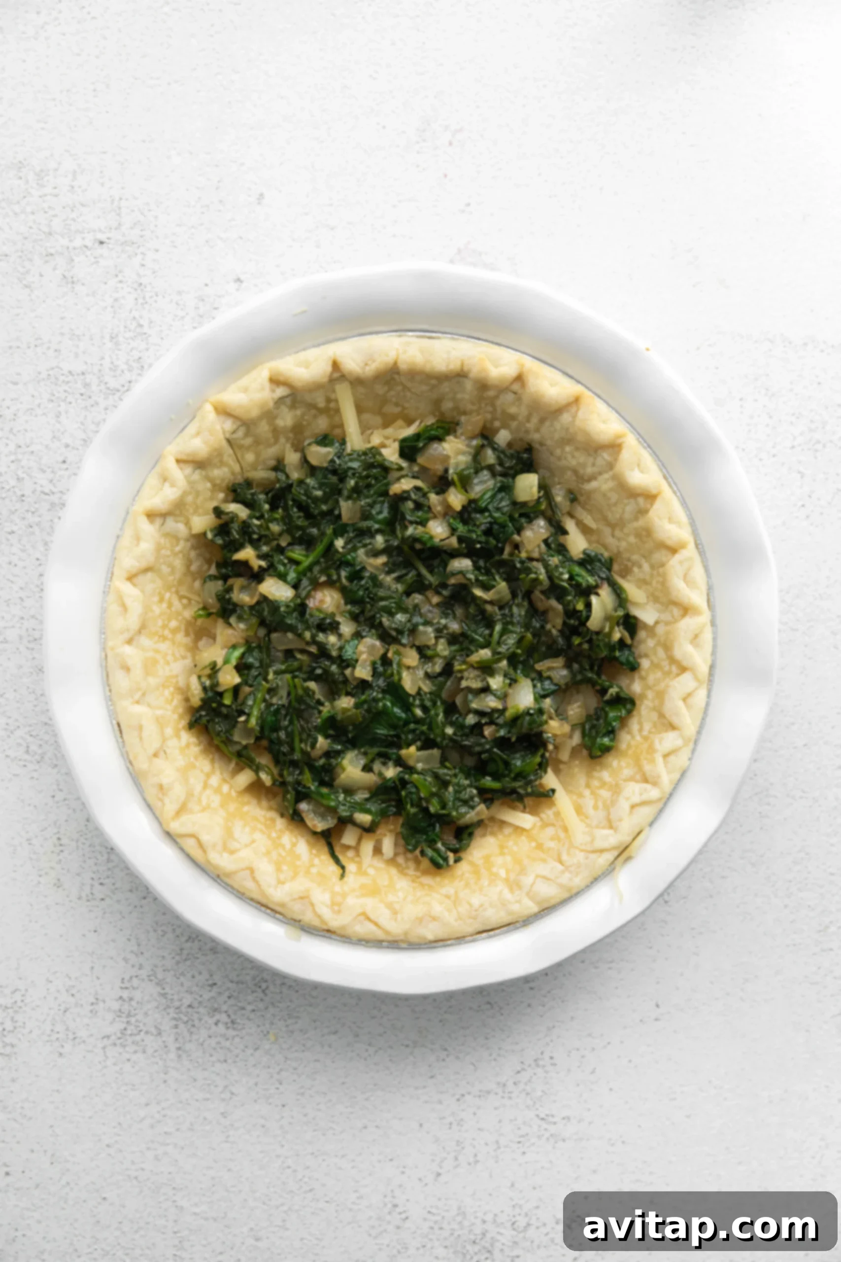 Sautéed spinach, onions, and garlic cooking in a large skillet, forming the aromatic base for the quiche filling.