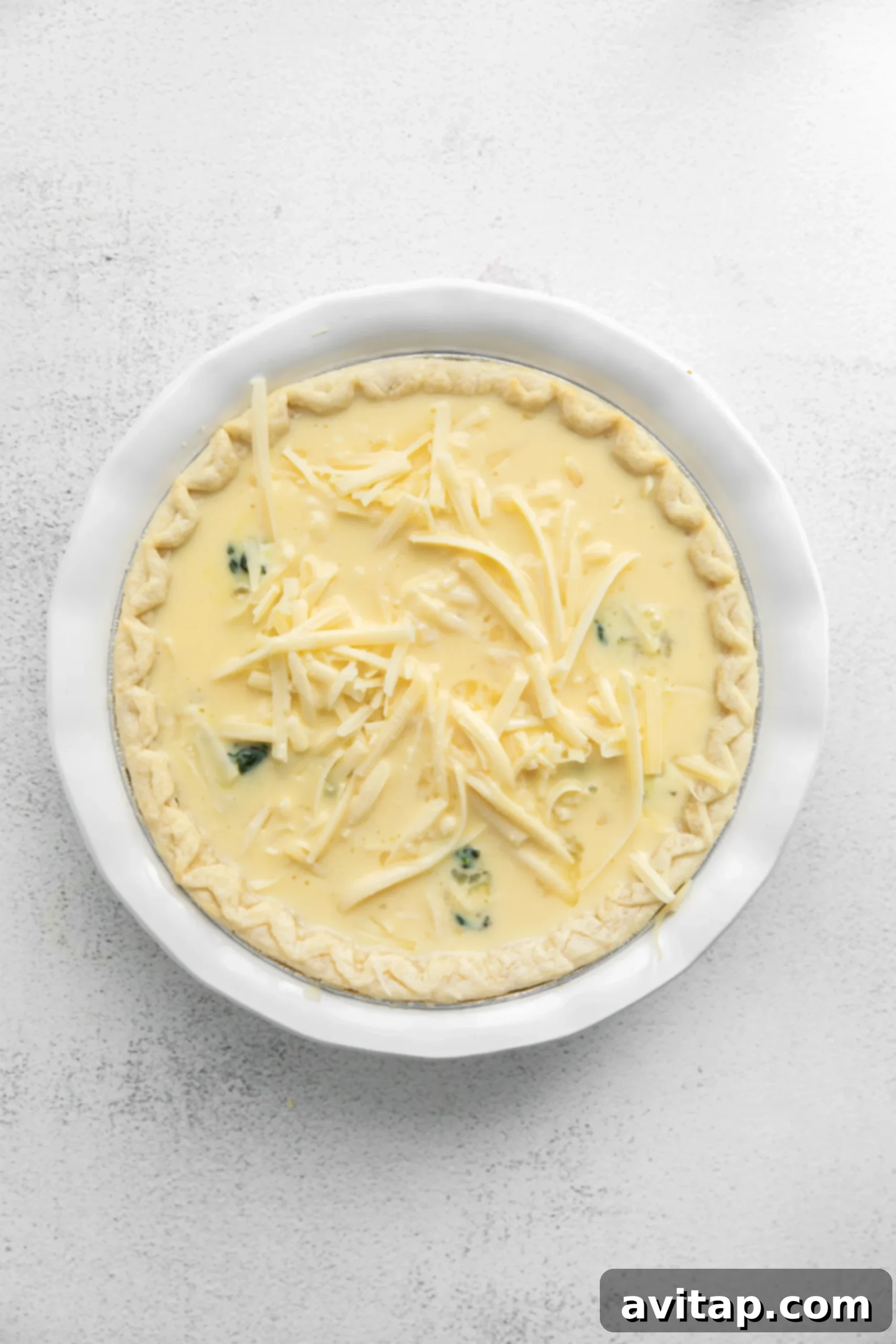 Close-up of shredded Gruyère cheese beautifully sprinkled on top of an unbaked spinach quiche, poised for baking.