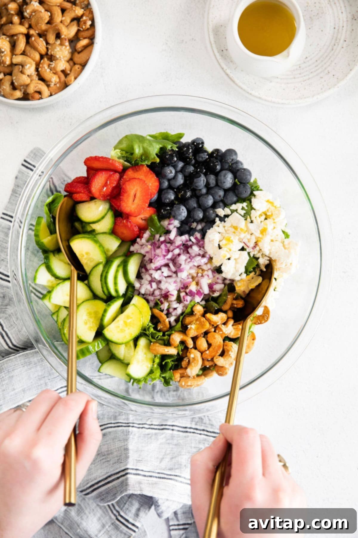 A colorful bowl filled with fresh spring mix salad ingredients, including blueberries, strawberries, cucumbers, and cashews.