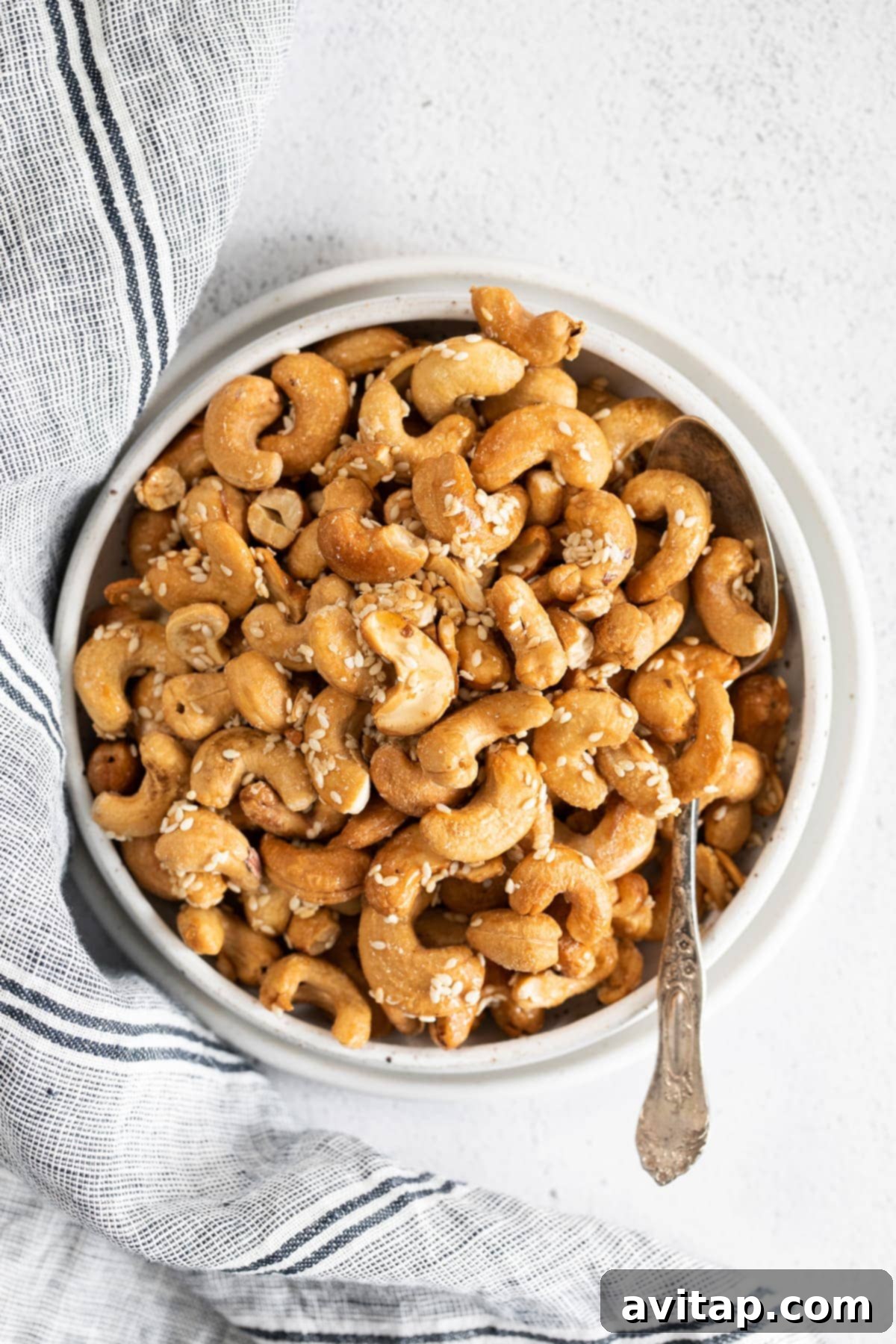 A close-up shot of a bowl filled with golden brown, sesame-roasted cashews.