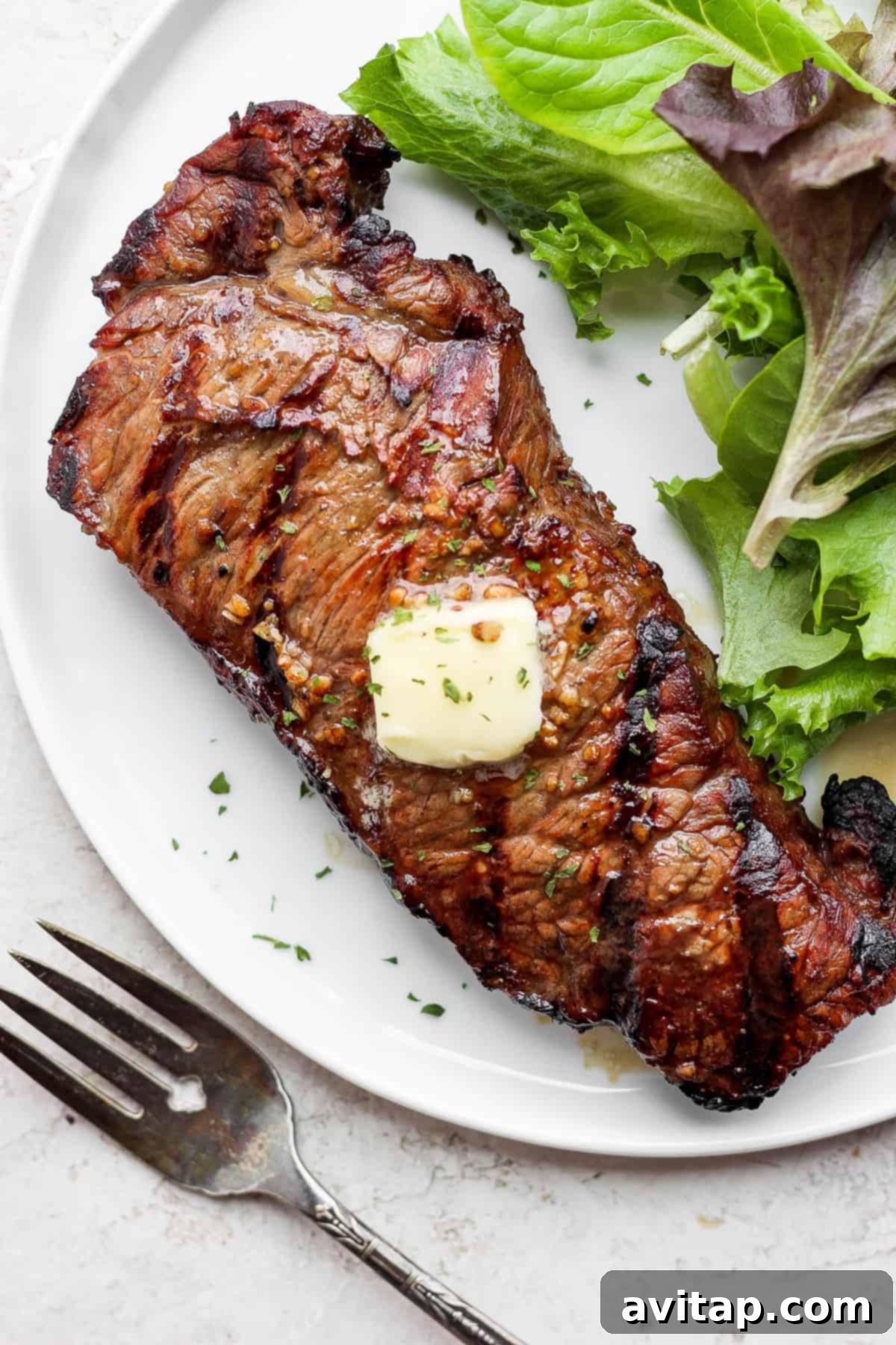 A perfectly grilled steak resting on a plate with melting butter, ready to be enjoyed.