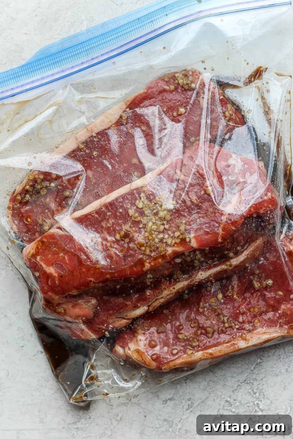 Four New York strip steaks marinating in a plastic bag, absorbing flavors.