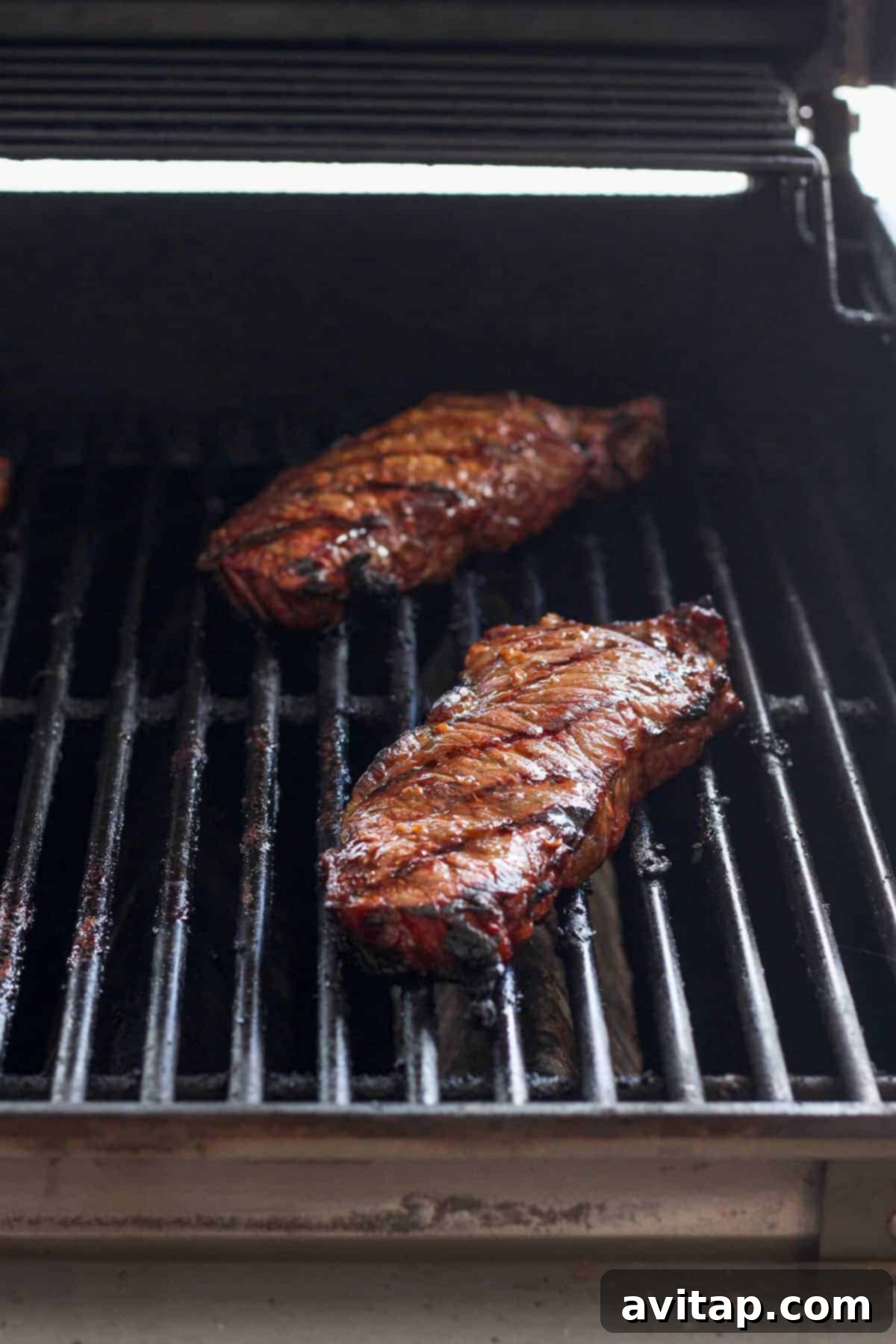 Gas grill with three steaks cooking on the grates, showing developing grill marks.
