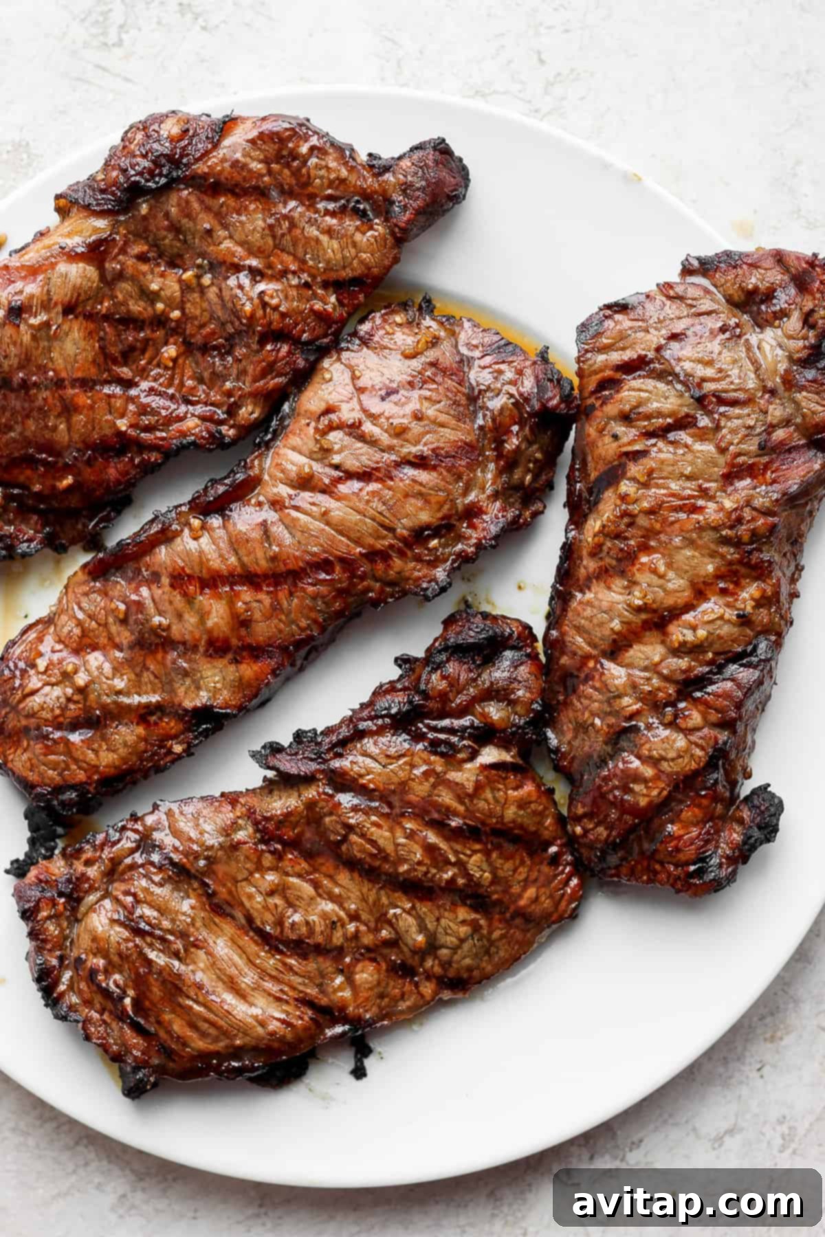 Four large, perfectly grilled steaks resting on a white platter, ready to be sliced.