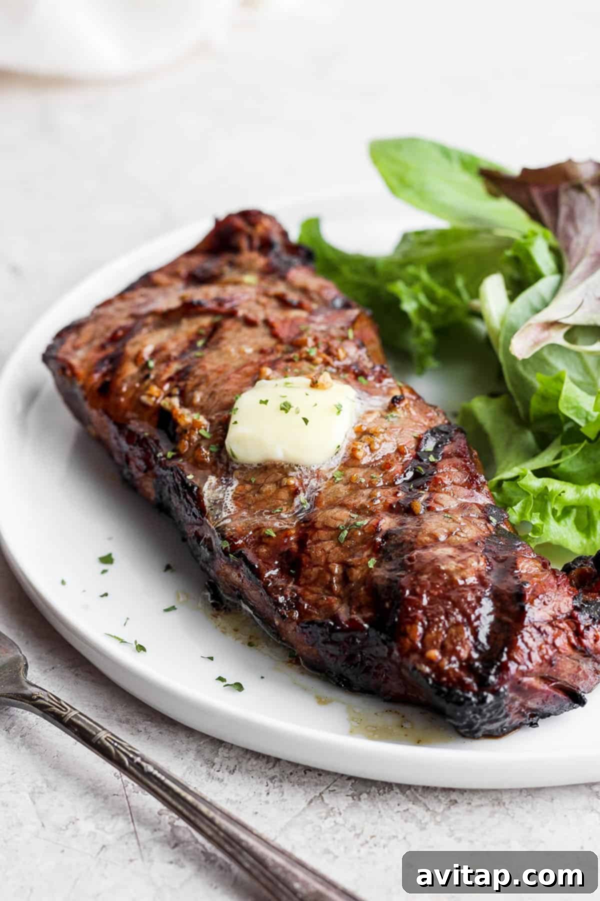 A sliced grilled steak served on a plate with fresh green salad.