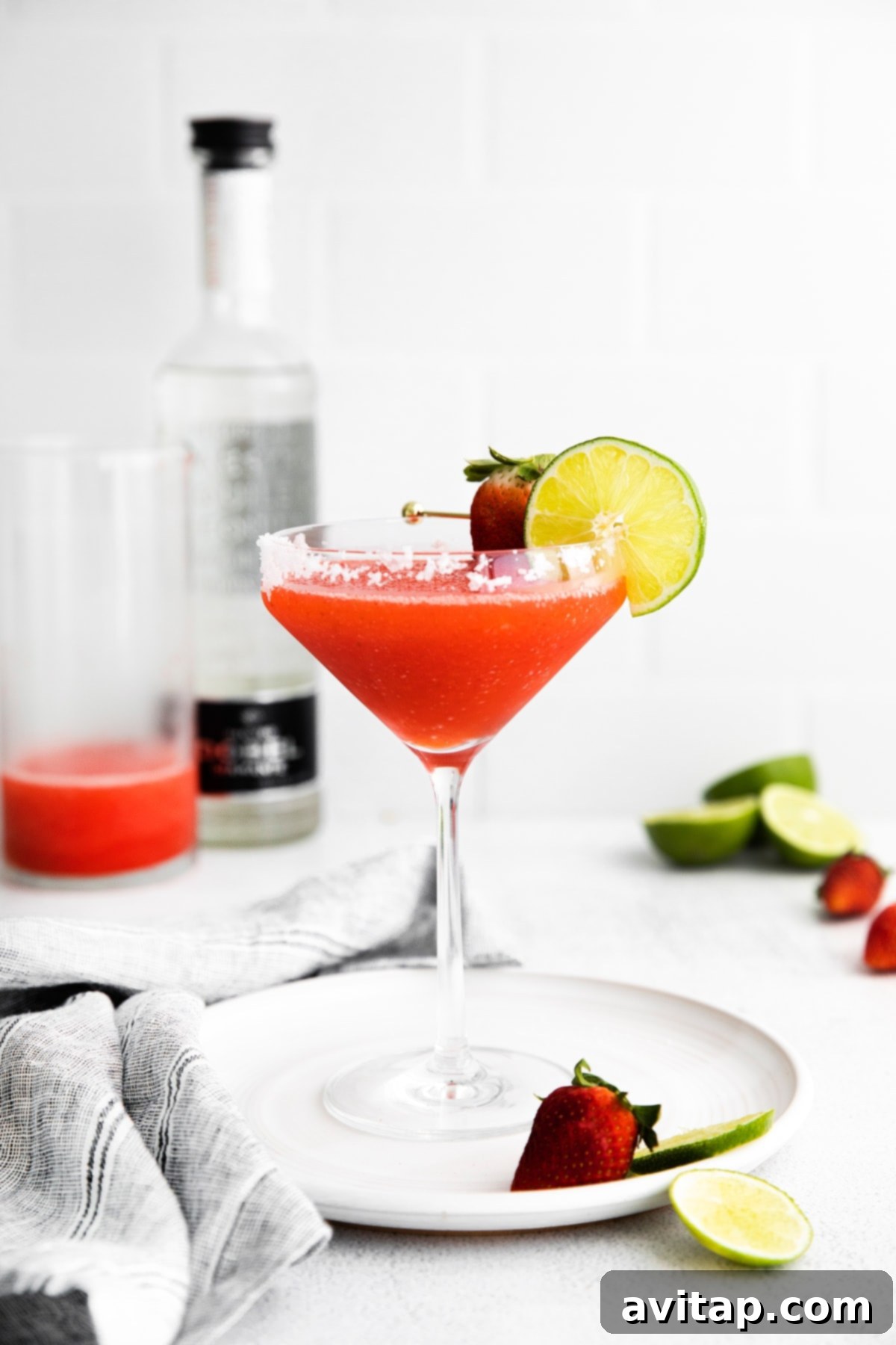 A frosty frozen strawberry margarita in a glass, with a lime wheel garnish, resting on a textured surface
