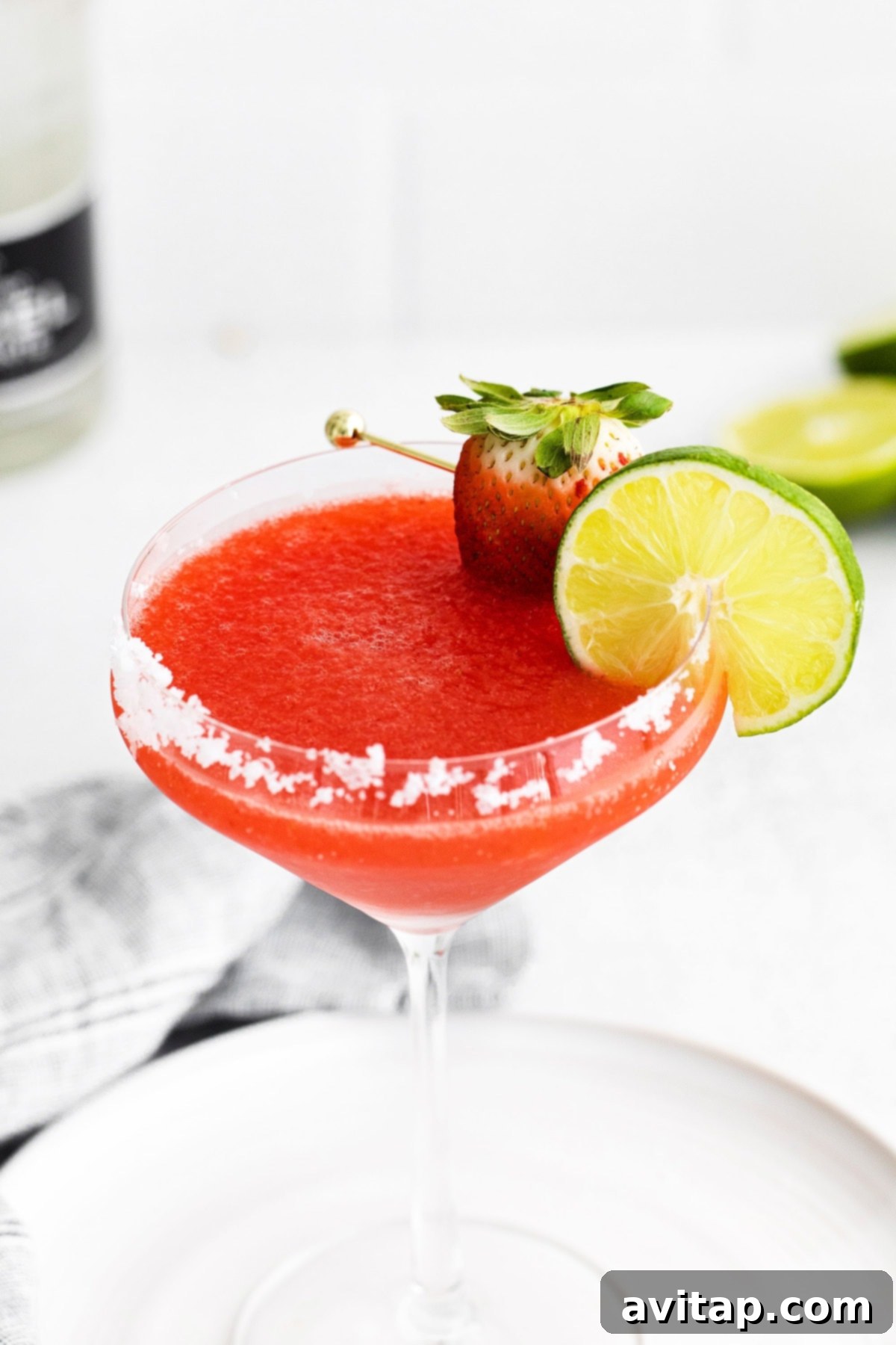 A beautifully presented frozen strawberry margarita in a glass with a perfectly salted rim and a lime wedge garnish