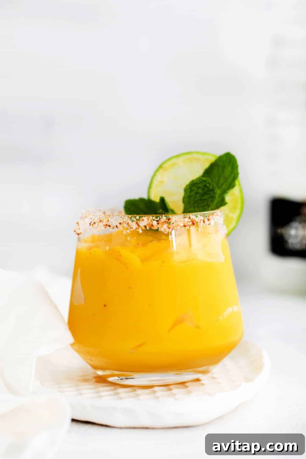 Sun-Drenched Mango Margarita 2 A vibrant frozen mango margarita in a glass, garnished with a fresh lime wedge and a hint of mint.