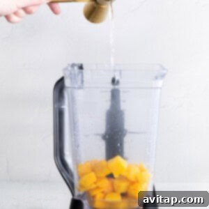 All margarita ingredients, including frozen mango and tequila, being poured into a blender pitcher, ready for blending.