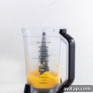 A vibrant, orange-hued frozen mango margarita being actively blended in a high-speed blender, showing a smooth, frosty texture.