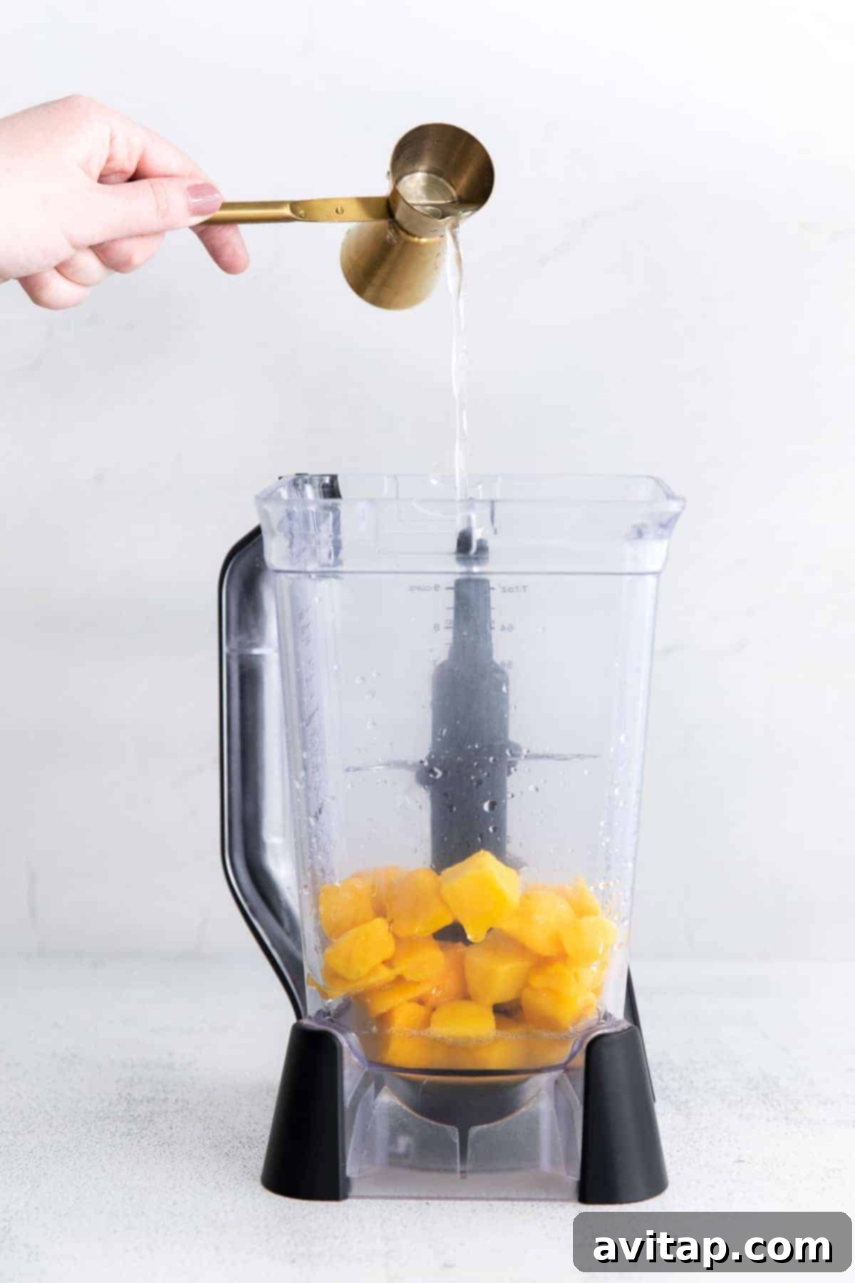 Sun-Drenched Mango Margarita 3 Pouring tequila into a blender filled with frozen mango chunks and other margarita ingredients, ready to be blended.