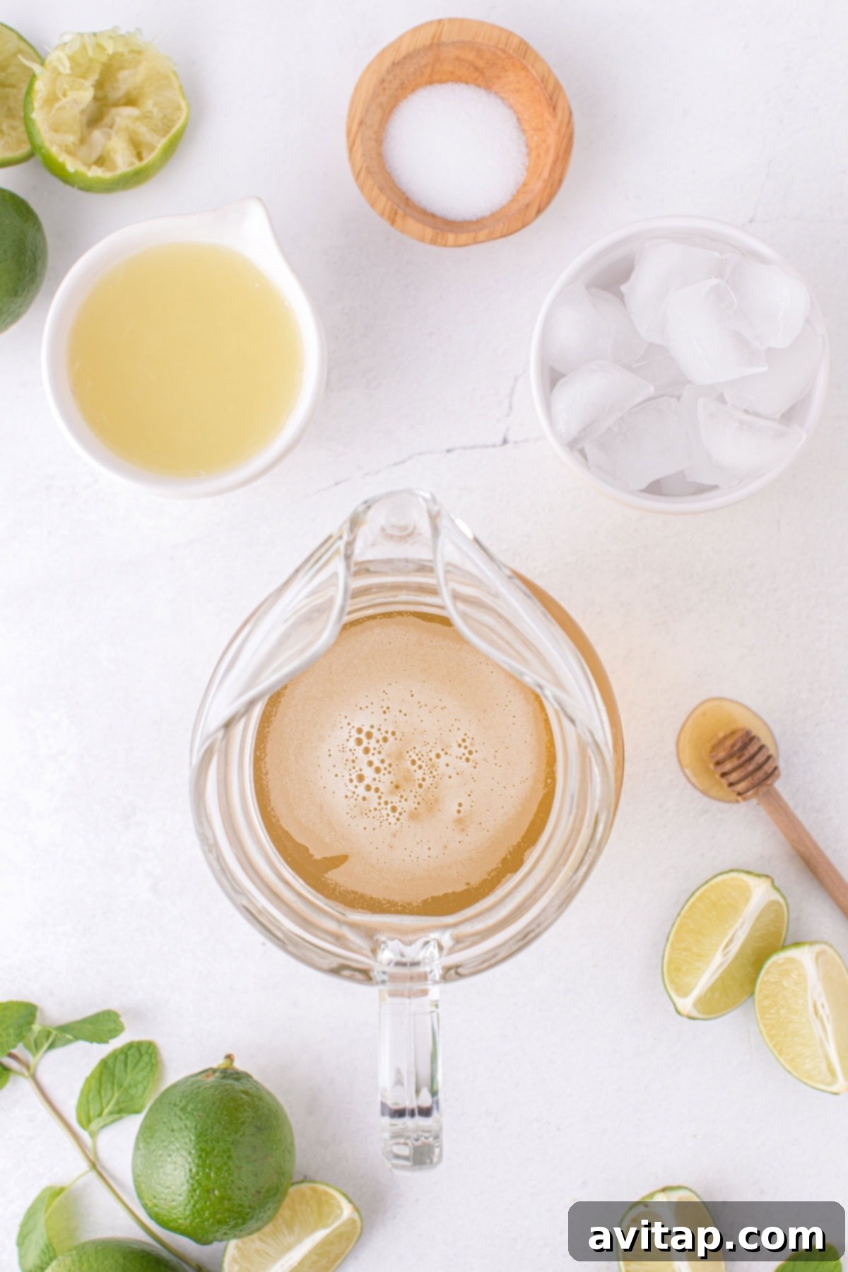 A pitcher filled with delicious homemade limeade and plenty of ice, adorned with fresh lime slices, sits alongside ingredients for the recipe, ready to be served at a gathering.
