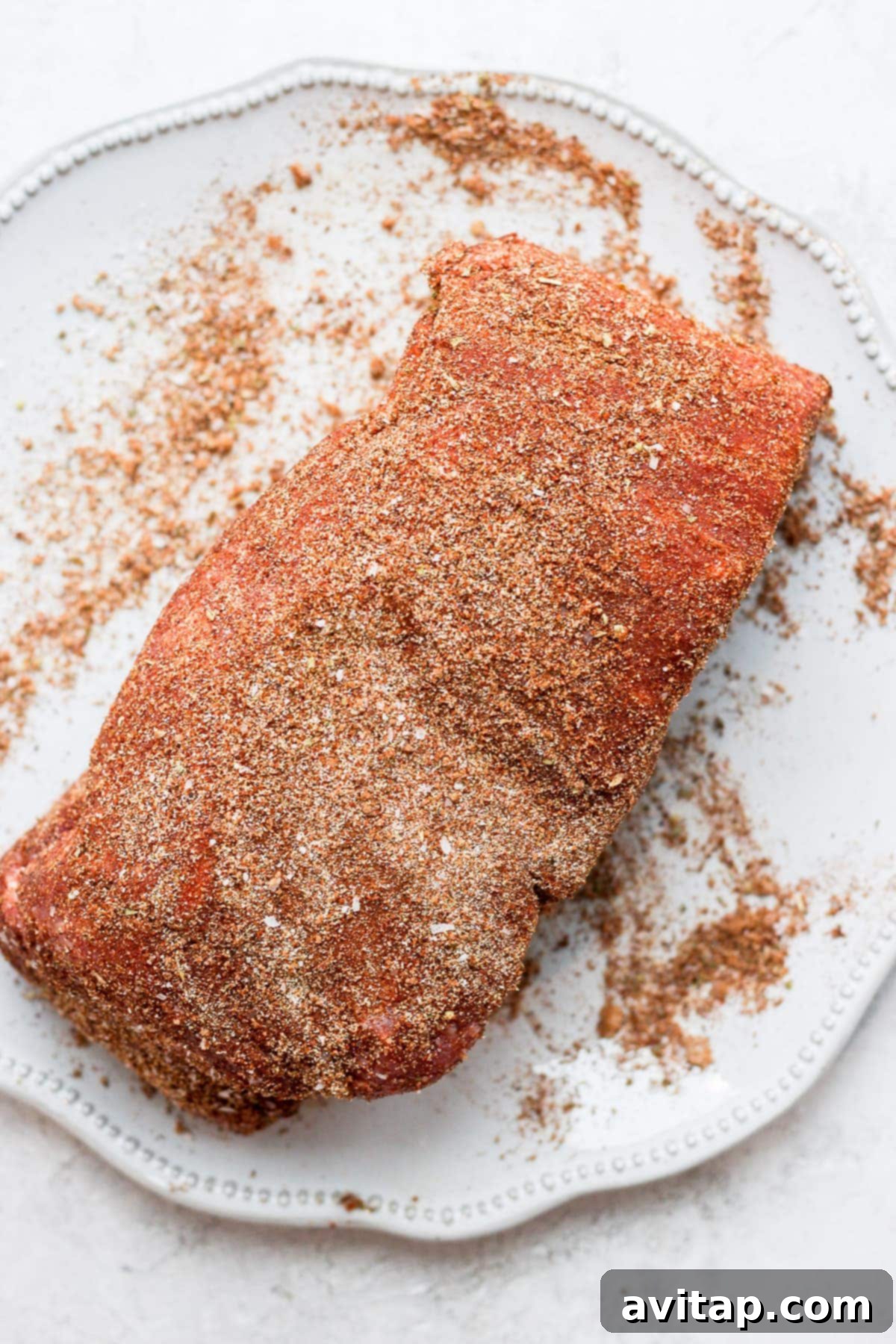 A raw pork roast generously coated with a rich dry rub of spices.
