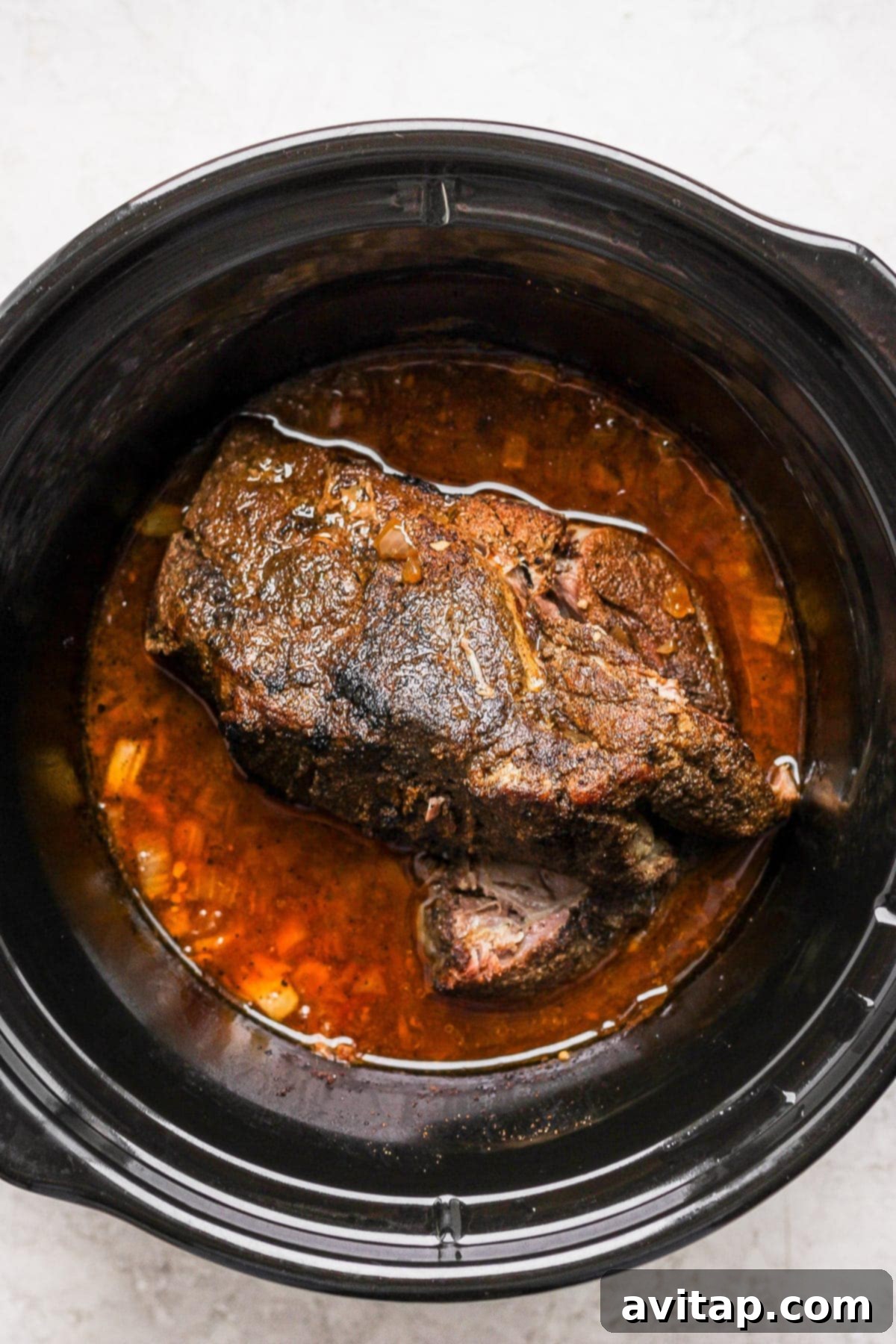 A seasoned pork roast submerged in liquid inside a slow cooker.