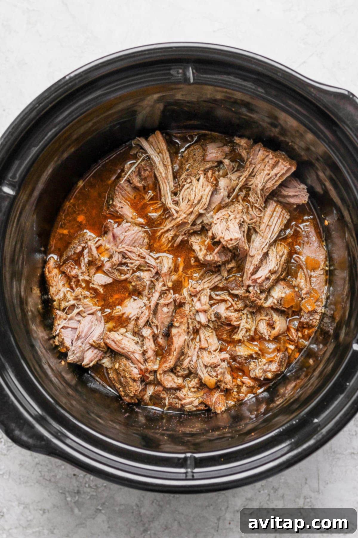 Shredded carnitas bathed in flavorful juices inside a slow cooker.