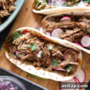 Close-up of crispy carnitas served on a cutting board with lime wedges and cilantro.